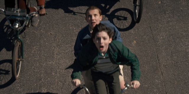 Wide shot frame from Stranger Things — street, bicycle, bird