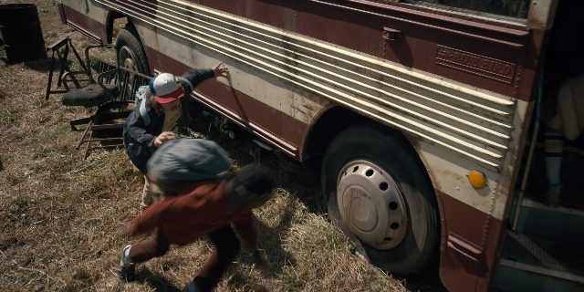 Wide shot frame from Stranger Things — standing, hat, chair