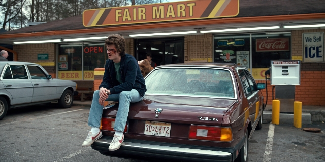 Wide shot frame from Stranger Things — sitting, plate, car