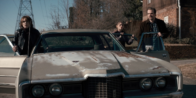 Wide shot frame from Stranger Things — standing, door, car