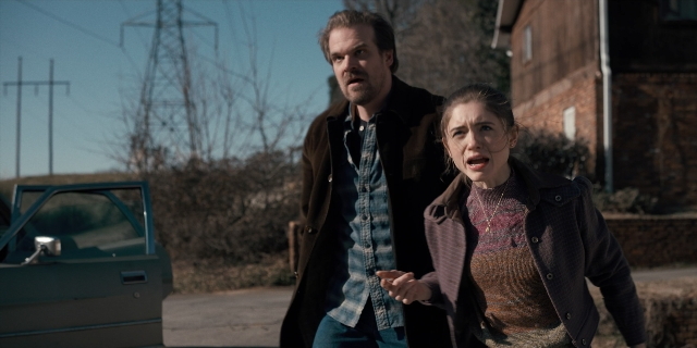 Wide shot frame from Stranger Things — walking, street, car