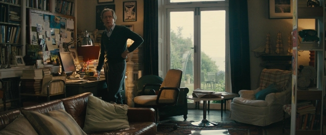 Wide shot frame from About Time — standing, room, table