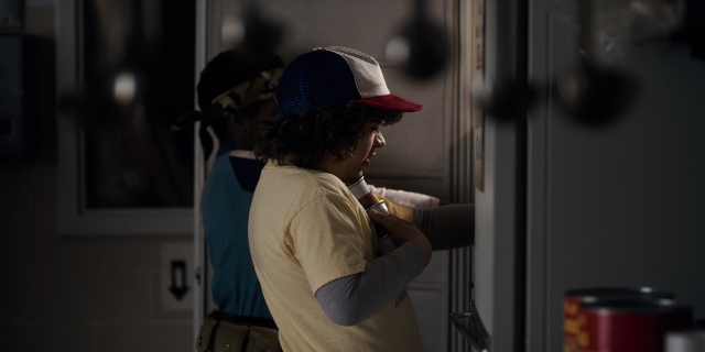 Wide shot frame from Stranger Things — standing, door, hat