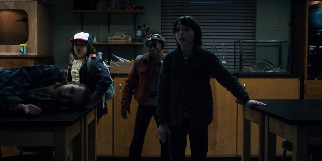Wide shot frame from Stranger Things — standing, room, table