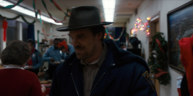 Wide shot frame from Stranger Things — standing, hat, mustache