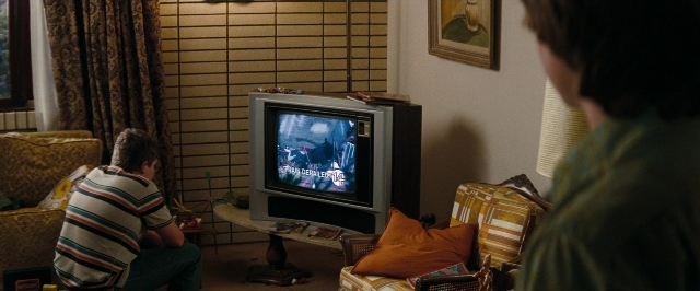 Wide shot frame from Super 8 — sitting, room, table