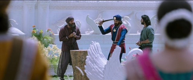 Wide shot frame from Bãhubali 2: The Conclusion — standing, dialogue, hat