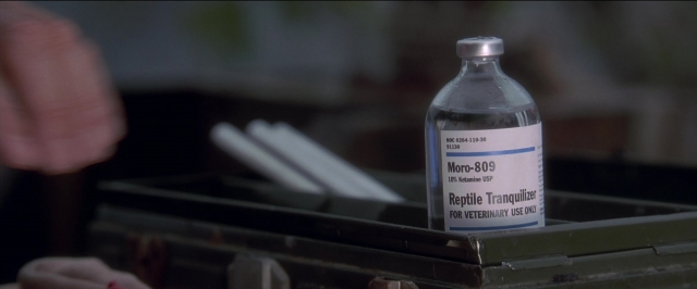 Frame from Anaconda — hat, bottle, glass