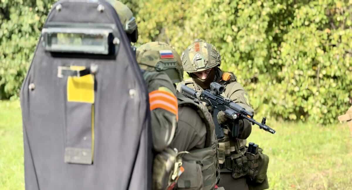 Вооружённый боец в шлеме действует за баллистическим щитом.