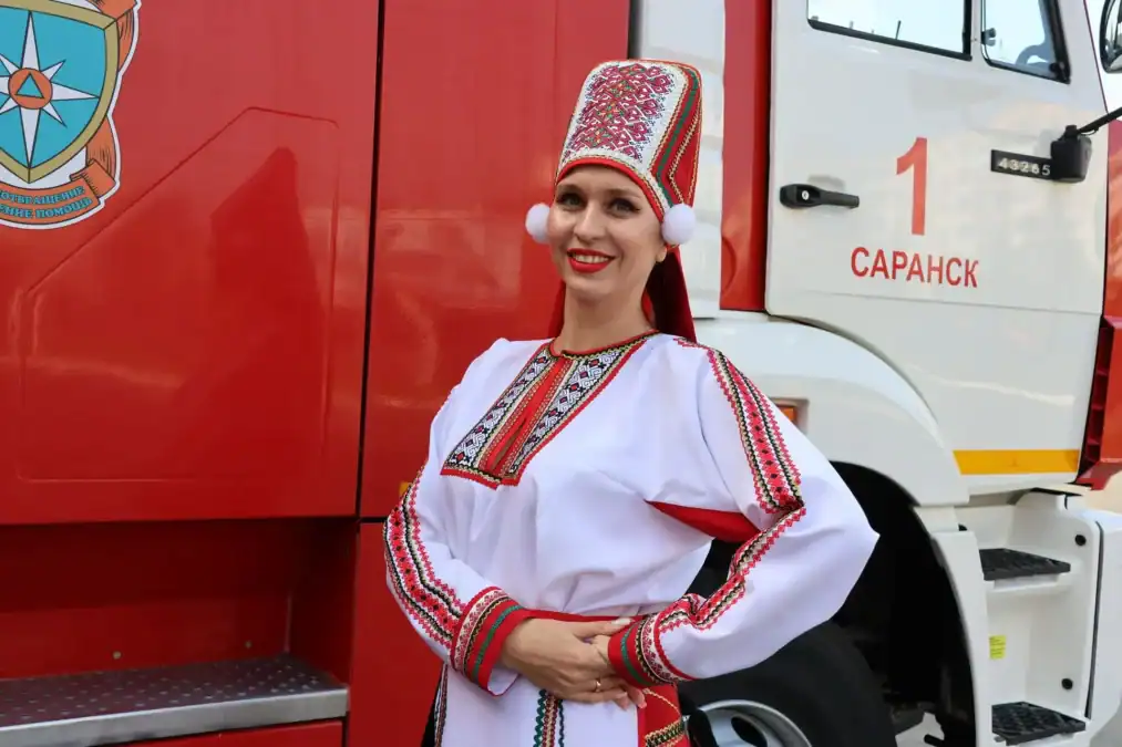 Женщина в национальном костюме позирует рядом с пожарной машиной.
