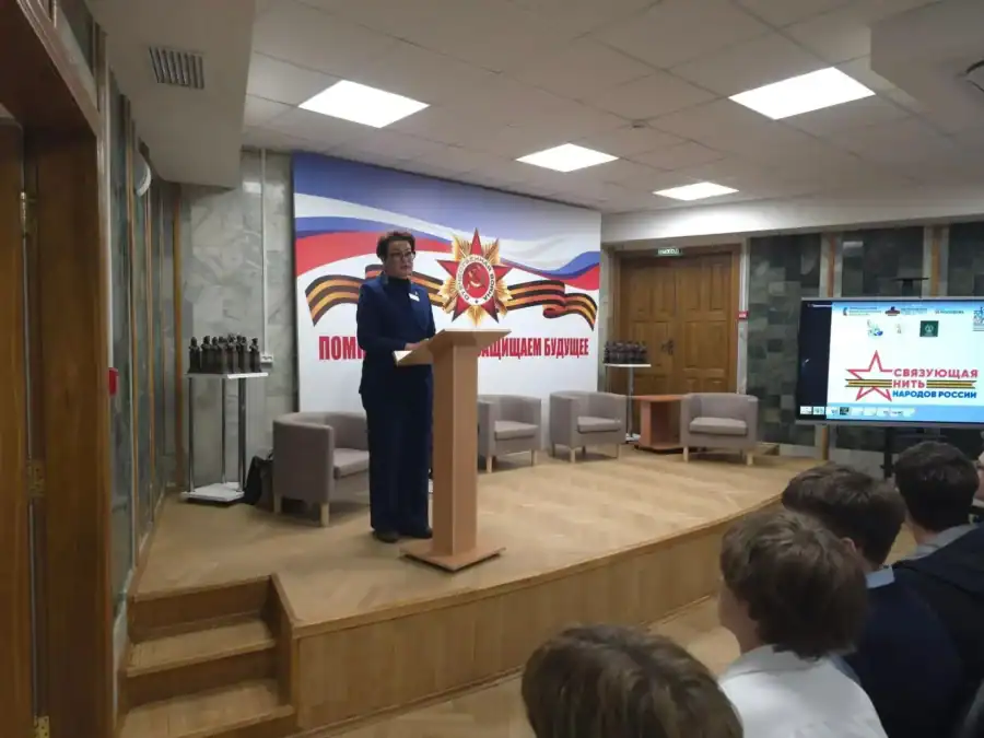 Женщина выступает за трибуной перед школьниками в музейном зале.