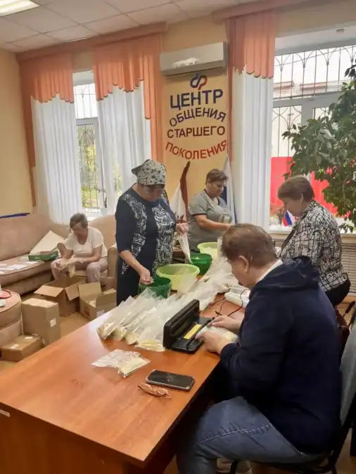 Женщины за столом фасуют продукты в пакеты рядом с коробками.