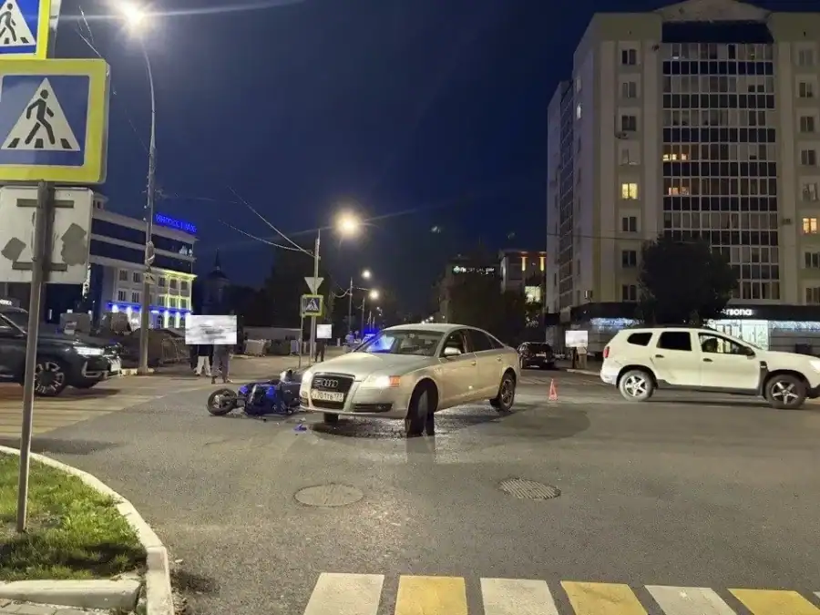 Автомобиль Audi и мопед находятся на ночном перекрёстке возле пешеходных переходов.