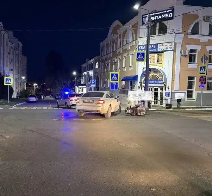 Автомобиль и мопед находятся у пешеходного перехода рядом с полицейской машиной.