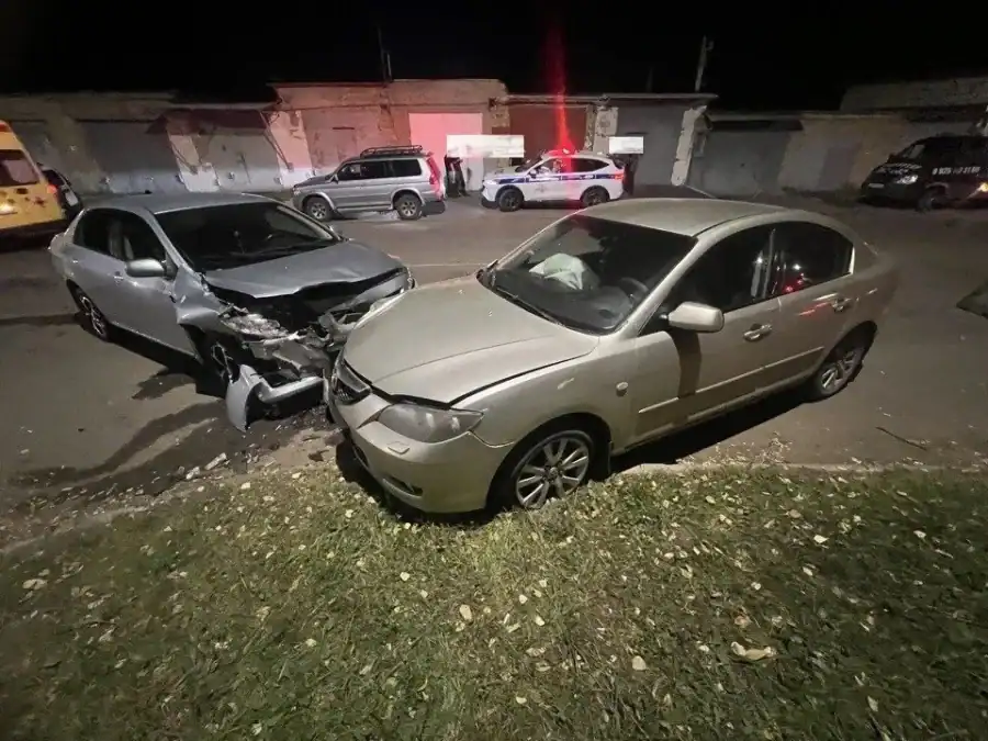 Два легковых автомобиля с повреждёнными передними частями стоят ночью у обочины.