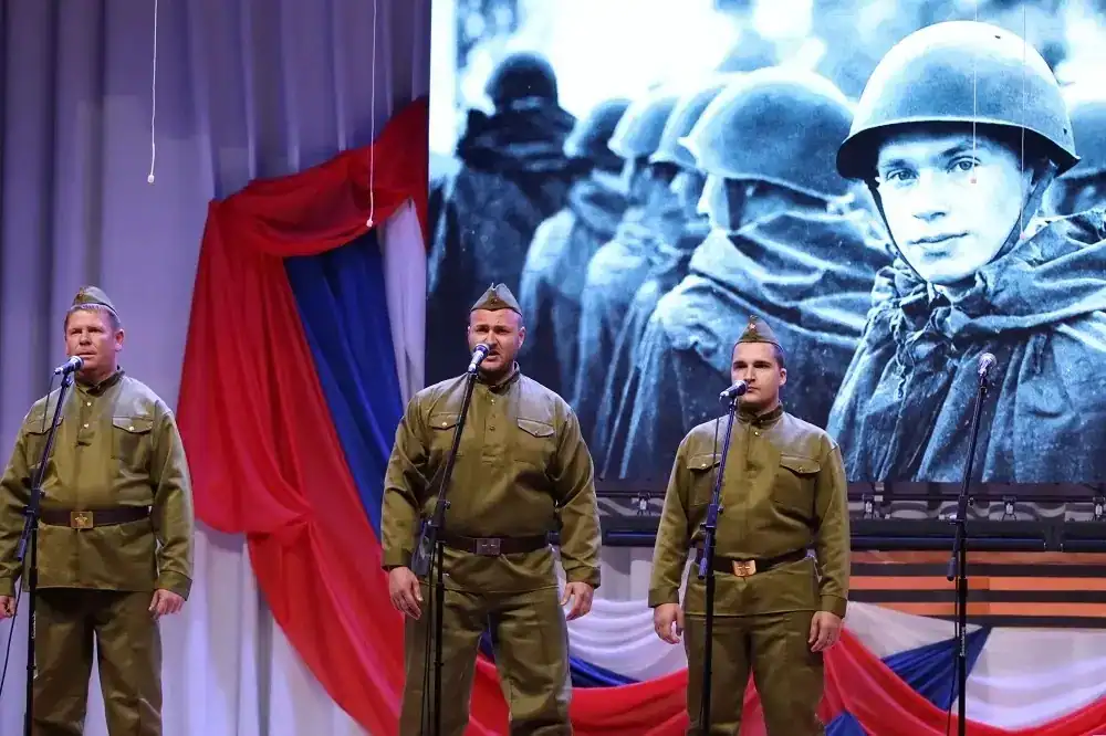 Трое мужчин в военной форме поют у микрофонов на сцене.