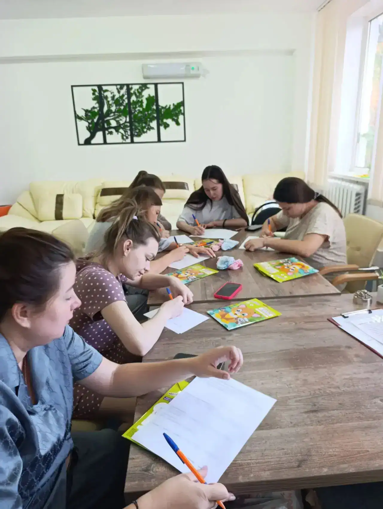 Несколько женщин за столом пишут и занимаются поделками из цветной бумаги.