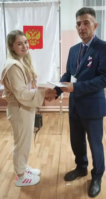 Девушка и мужчина обмениваются документом на избирательном участке.