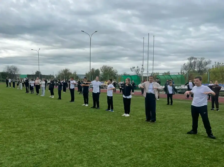 Школьники выполняют упражнения, выстроившись рядами на футбольном поле.