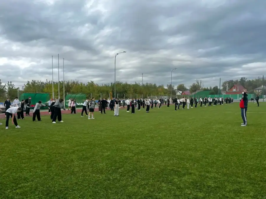 Большая группа школьников разминается на поле спортивного стадиона.