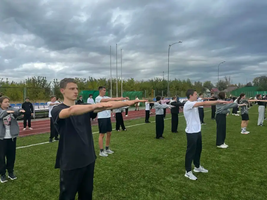 Школьники выполняют упражнение с вытянутыми вперёд руками на поле.