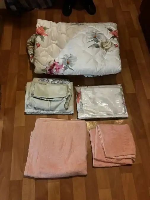 Одеяло с цветочным рисунком, сложенный текстиль и розовые полотенца на полу.