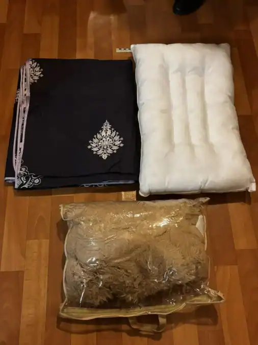 На полу разложены тёмный текстиль, белая подушка и упакованное объёмное изделие.