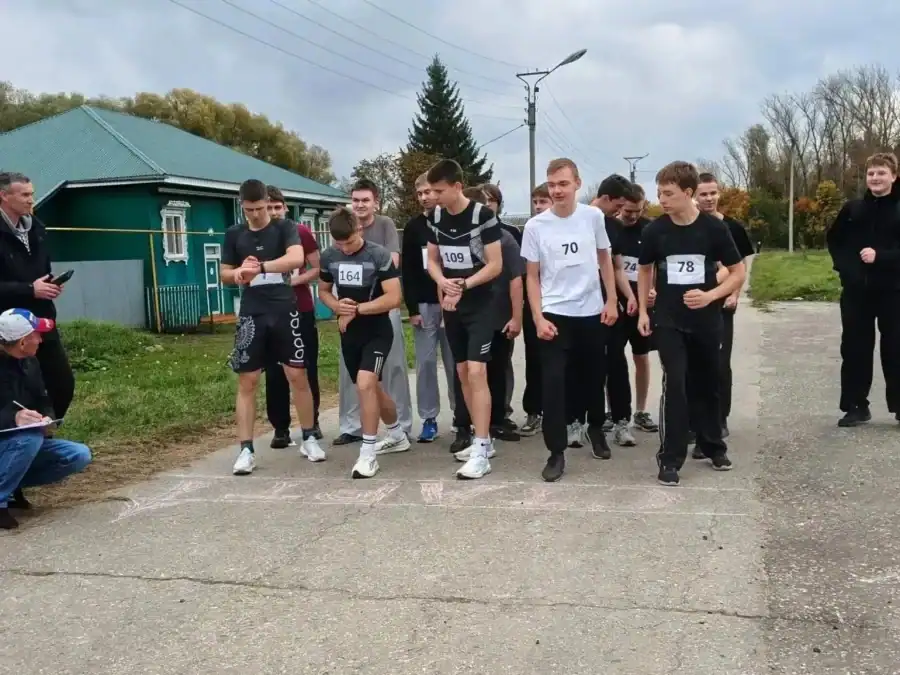 Юноши с нагрудными номерами готовятся к старту у линии на дороге.