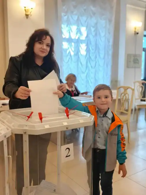 Женщина и мальчик опускают бюллетень в ящик на избирательном участке.