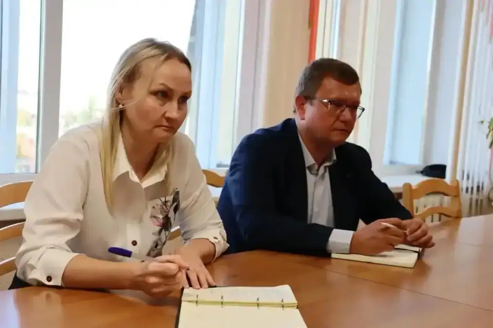 Двое участников встречи сидят за столом с блокнотами и ручками.