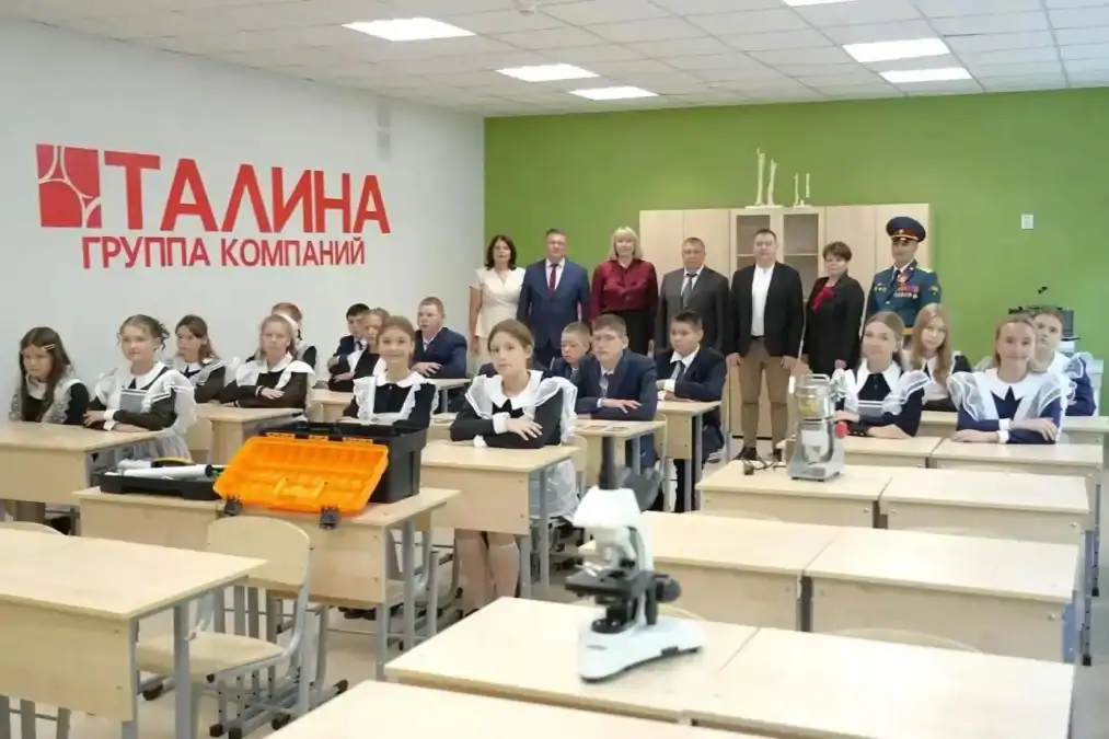 Школьники в форме сидят в классе с лабораторным оборудованием, взрослые стоят позади.