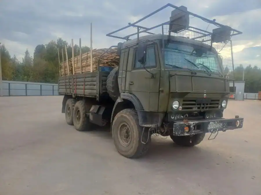Грузовой автомобиль с деревянными пиломатериалами стоит на площадке.
