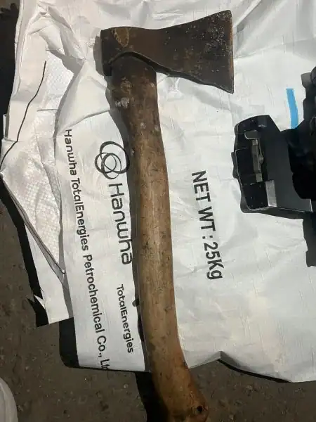Топор лежит на белом полипропиленовом мешке рядом с чёрным предметом.