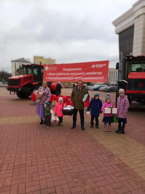Семья с детьми стоит между красной сельскохозяйственной техникой.