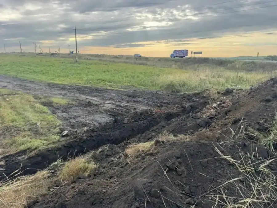 Траншея и отвалы грунта на обочине полевой дороги у трассы.