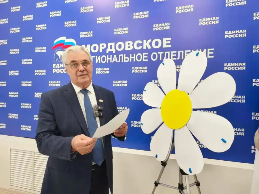 Мужчина держит лепесток рядом с большой ромашкой на стойке.