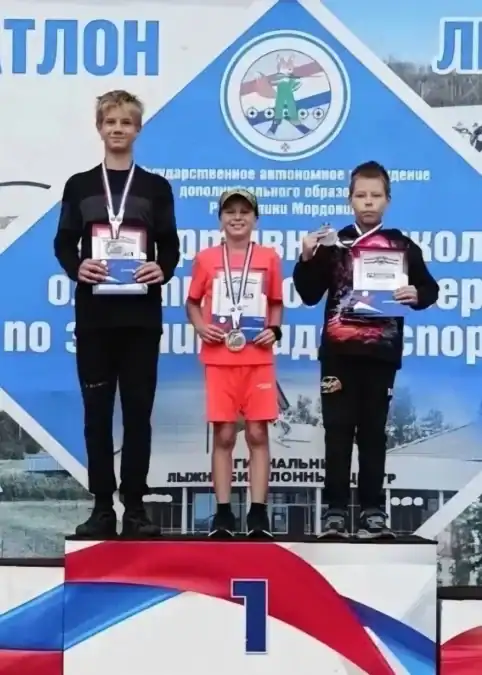 Три юных спортсмена с медалями и грамотами стоят на пьедестале.