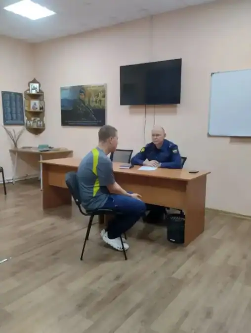 Сотрудник в форменной одежде беседует с мужчиной за столом в кабинете.