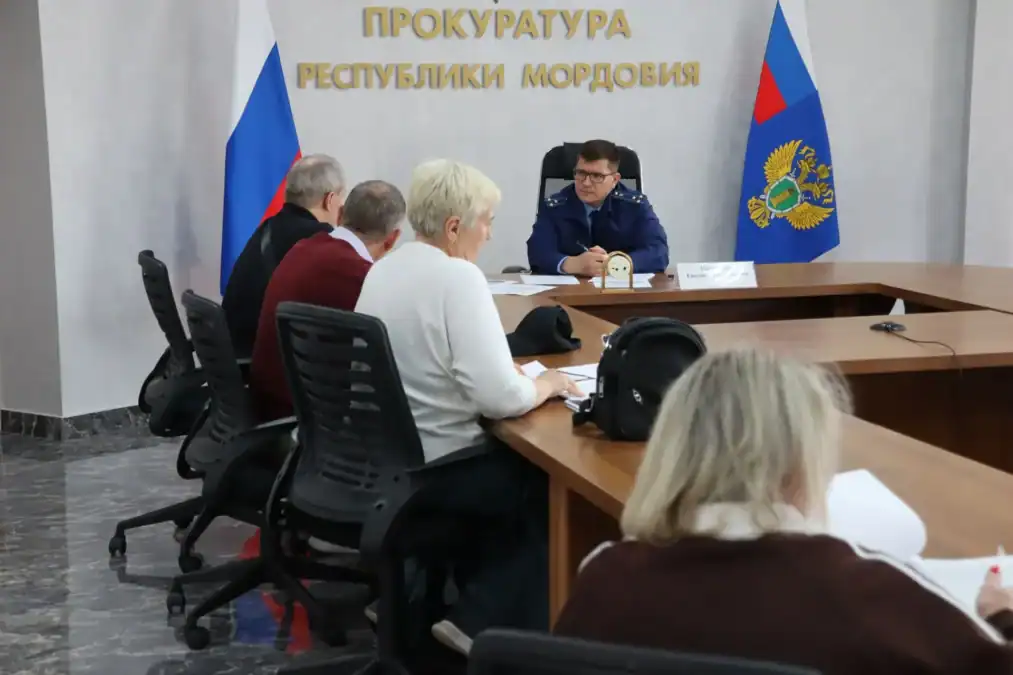 Сотрудник прокуратуры проводит прием нескольких посетителей за столом.