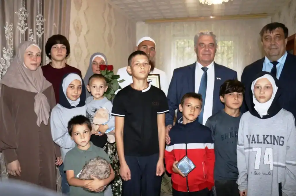 Многодетная семья с детьми и двумя мужчинами позирует в комнате с букетом.