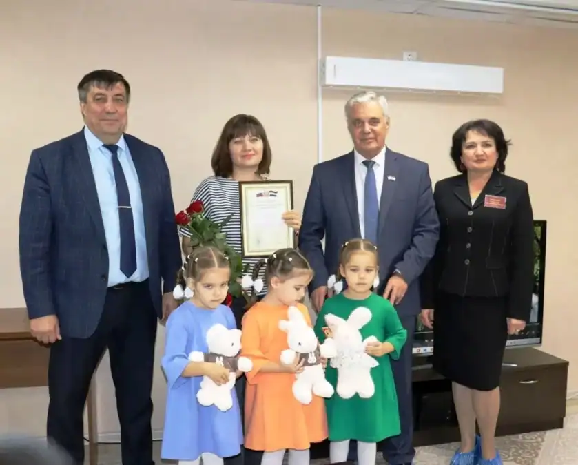 Три девочки с мягкими игрушками стоят рядом с родителями и гостями.