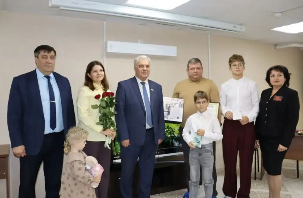 Семья с детьми, цветами и подарками позирует вместе с официальными гостями.