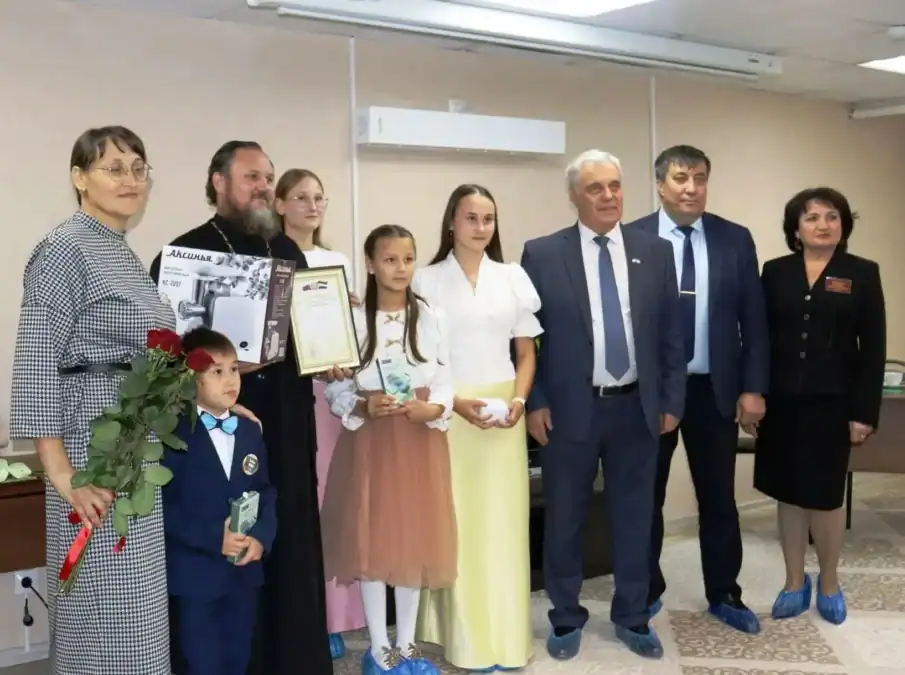 Семья с детьми и официальными гостями стоит рядом с благодарственным письмом и цветами.