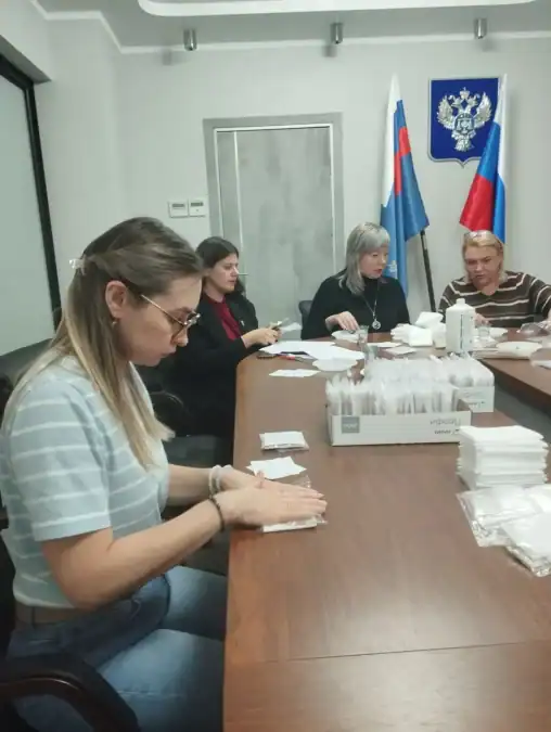 Женщины за длинным столом упаковывают материалы в индивидуальные комплекты.