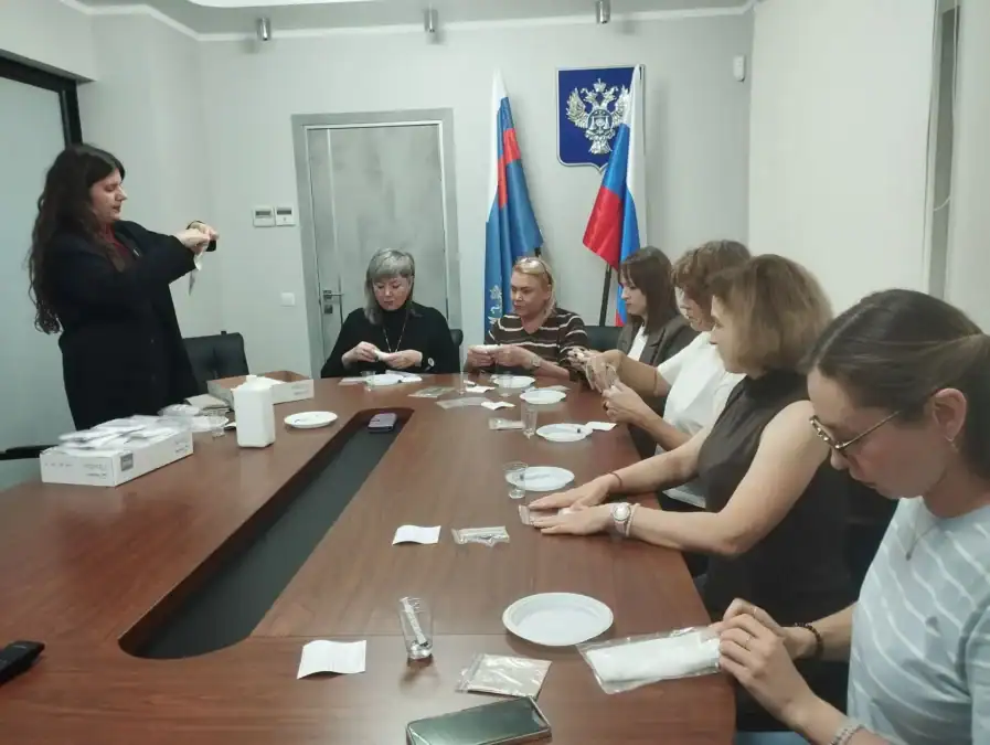 Семь сотрудниц за столом собирают и упаковывают наборы из салфеток и пакетов.
