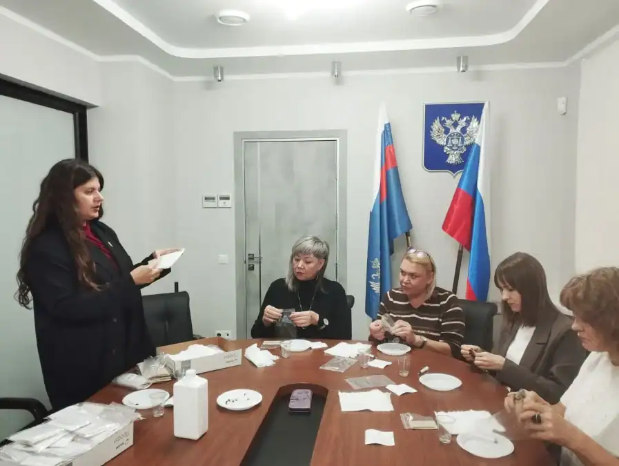 Сотрудницы за столом собирают комплекты, одна женщина показывает предмет в руках.