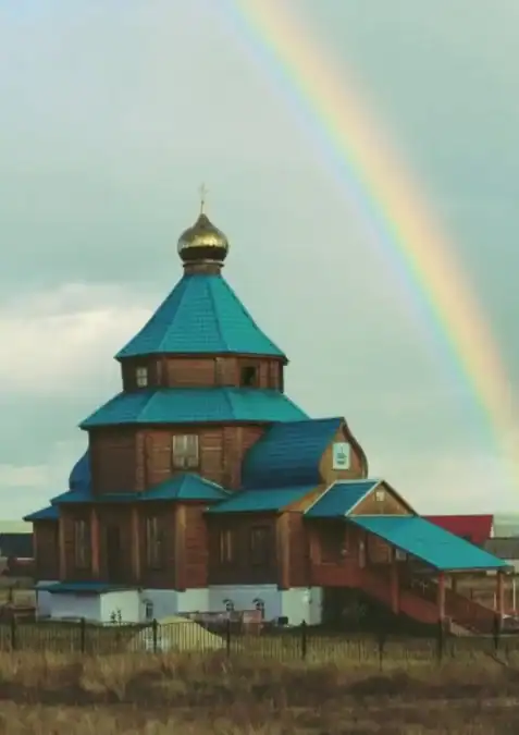 Деревянная церковь с бирюзовой крышей и радугой в небе.