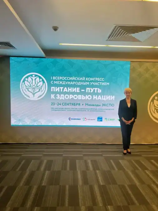 Участница конгресса стоит у экрана с названием мероприятия о здоровом питании.