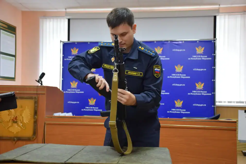 Сотрудник службы судебных приставов в форме осматривает автомат в помещении.