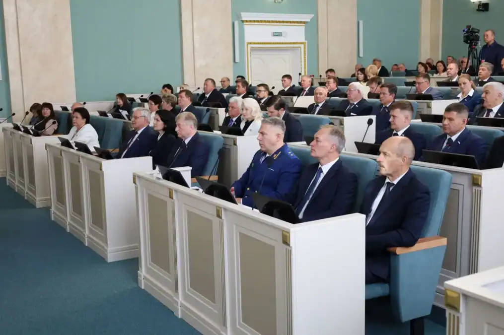 Депутаты в деловых костюмах сидят в зале заседаний регионального парламента.